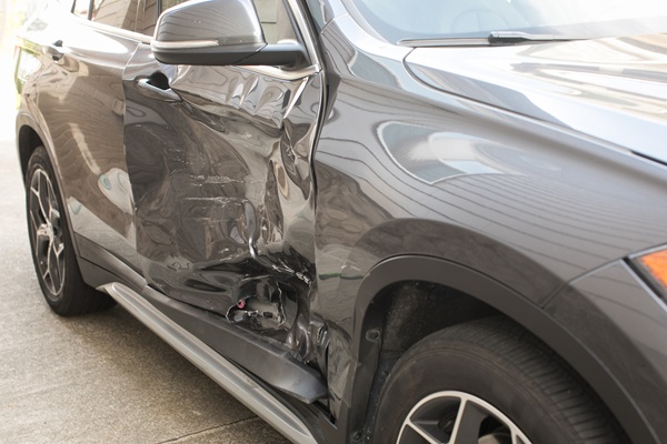 Dark-colored SUV with severe damage to the driver's side door and frame after a left-turn collision.