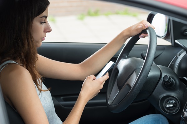 Driver texting on a cellphone while operating a vehicle, showing distracted driving behavior that increases crash risk and can create liability in car accident claims.